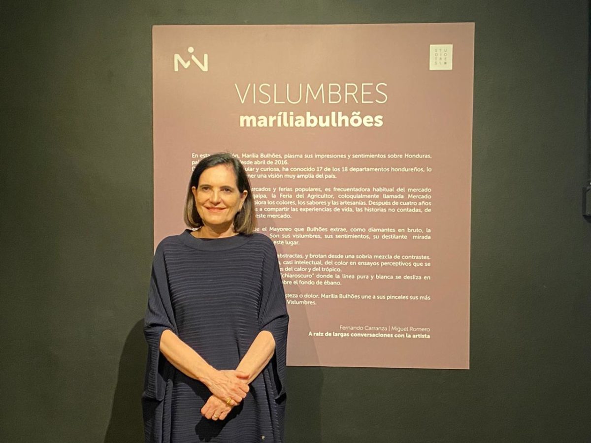 A artista plástica Marília Bulhões em frente ao texto da curadoria da Exposição Vislumbres em Honduras