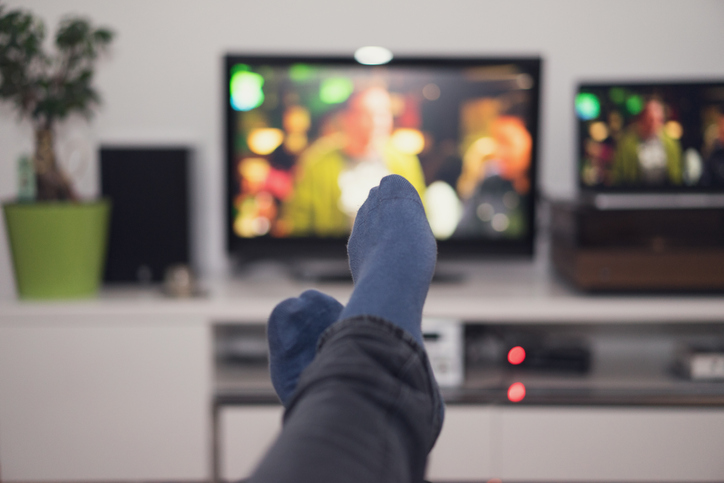 Person having feet up under blanket and watching TV