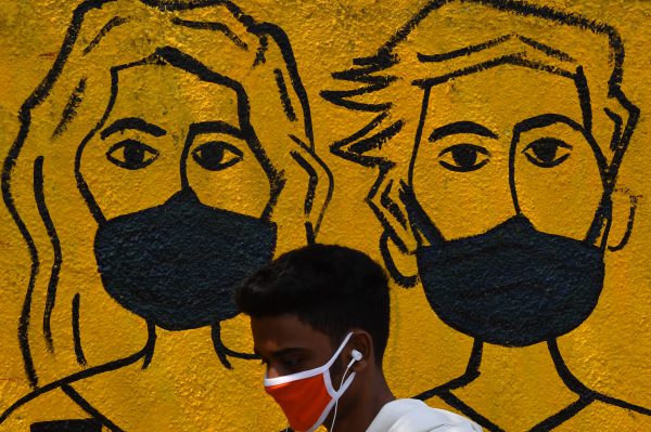 A youth wearing a facemask walk past a mural depicting people wearing famcemaks during the first day of a 21-day government-imposed nationwide lockdown as a preventive measure against the COVID-19 coronavirus, in Mumbai on March 25, 2020. - India's billion-plus population went into a three-week lockdown on March 25, with a third of the world now under orders to stay indoors, as the coronavirus pandemic forced Japan to postpone the Olympics until next year. (Photo by INDRANIL MUKHERJEE / AFP)