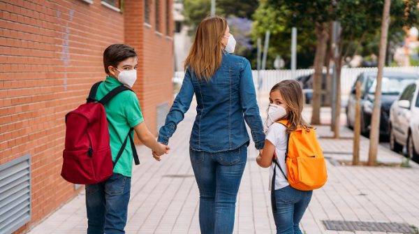 Mother walking with her children, boy and girl, go to school wearing masks during the coronavirus pandemic